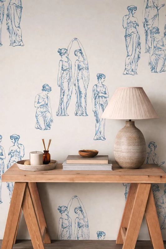 a wooden table with a lamp, books, and a bowl on it, set against a wall with a wallpaper depicting classical women.