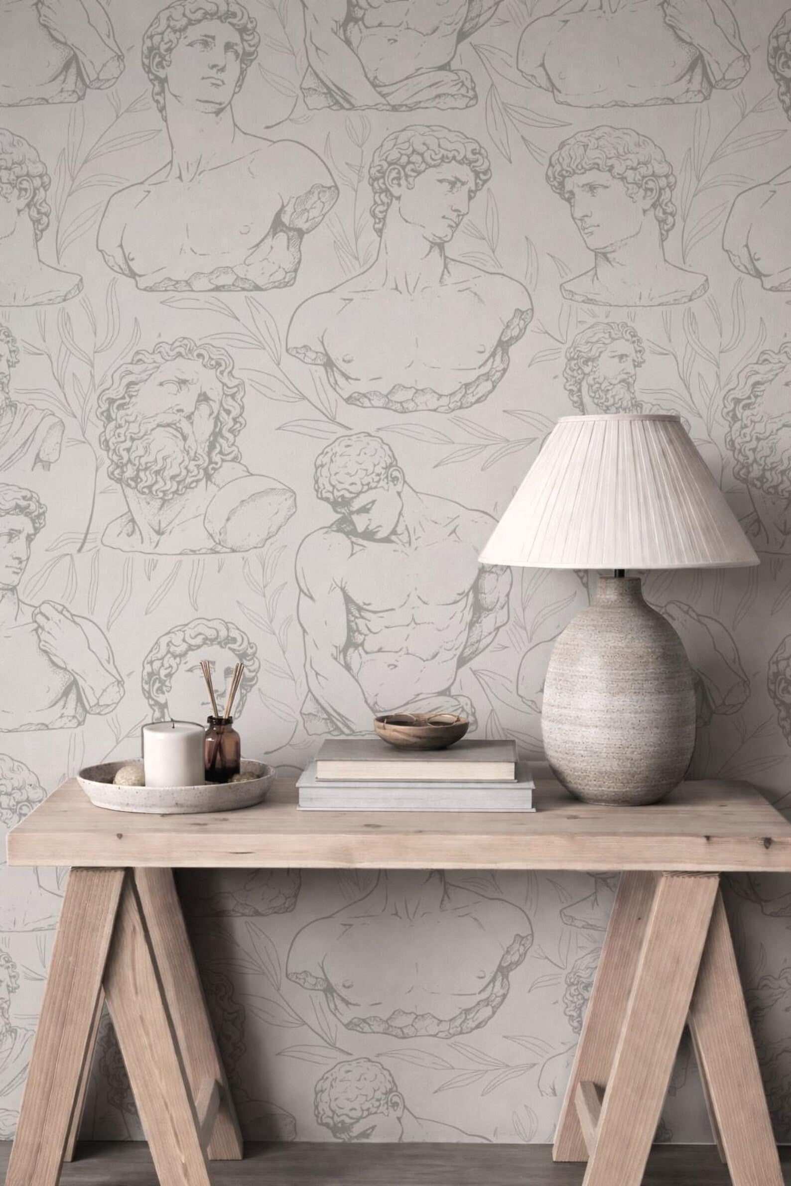 a wooden table with a lamp, a bowl, and some books on it, set against a wall with a repeating pattern of classical human anatomy drawings.
