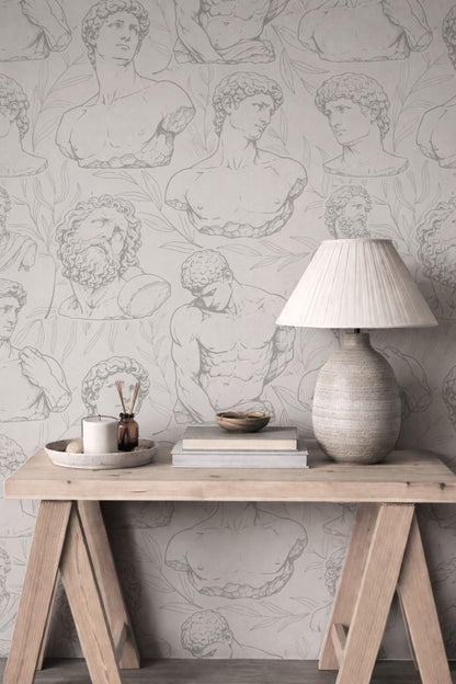 a wooden table with a lamp, a bowl, and some books on it, set against a wall with a repeating pattern of classical human anatomy drawings.