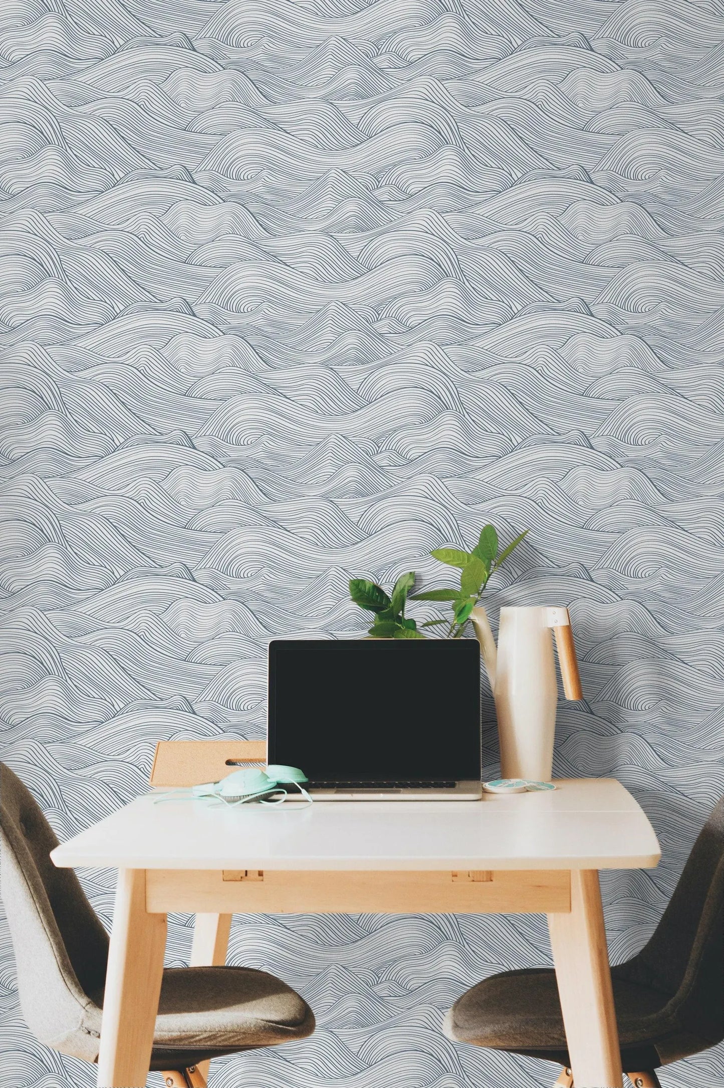 a modern workspace with a laptop on a white desk, a plant, and a vase, all set against a wall with a wave-patterned wallpaper.