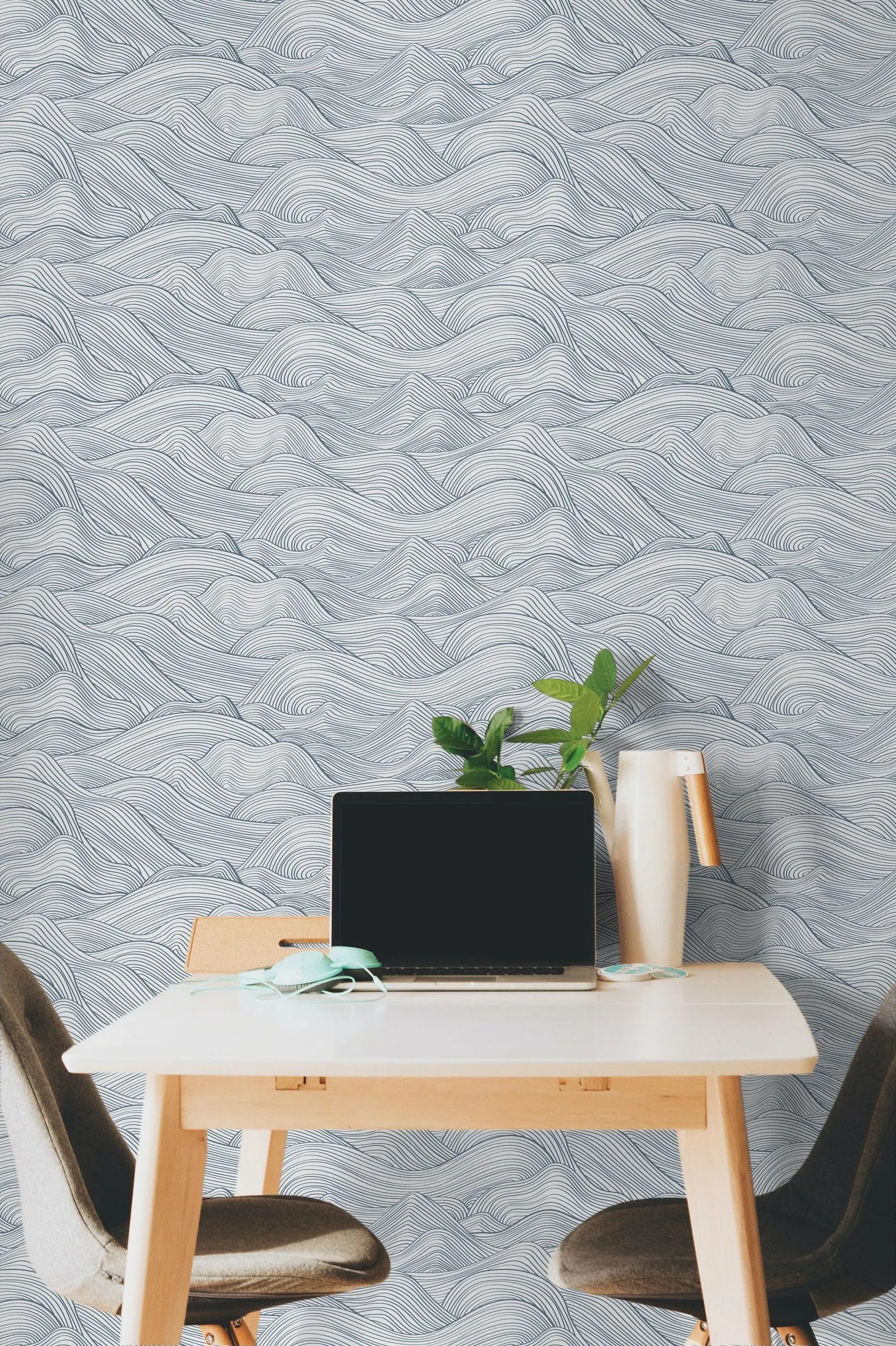 a modern workspace with a laptop on a white desk, a plant, and a vase, all set against a wall with a wave-patterned wallpaper.