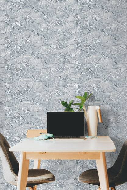 a modern workspace with a laptop on a white desk, a plant, and a vase, all set against a wall with a wave-patterned wallpaper.