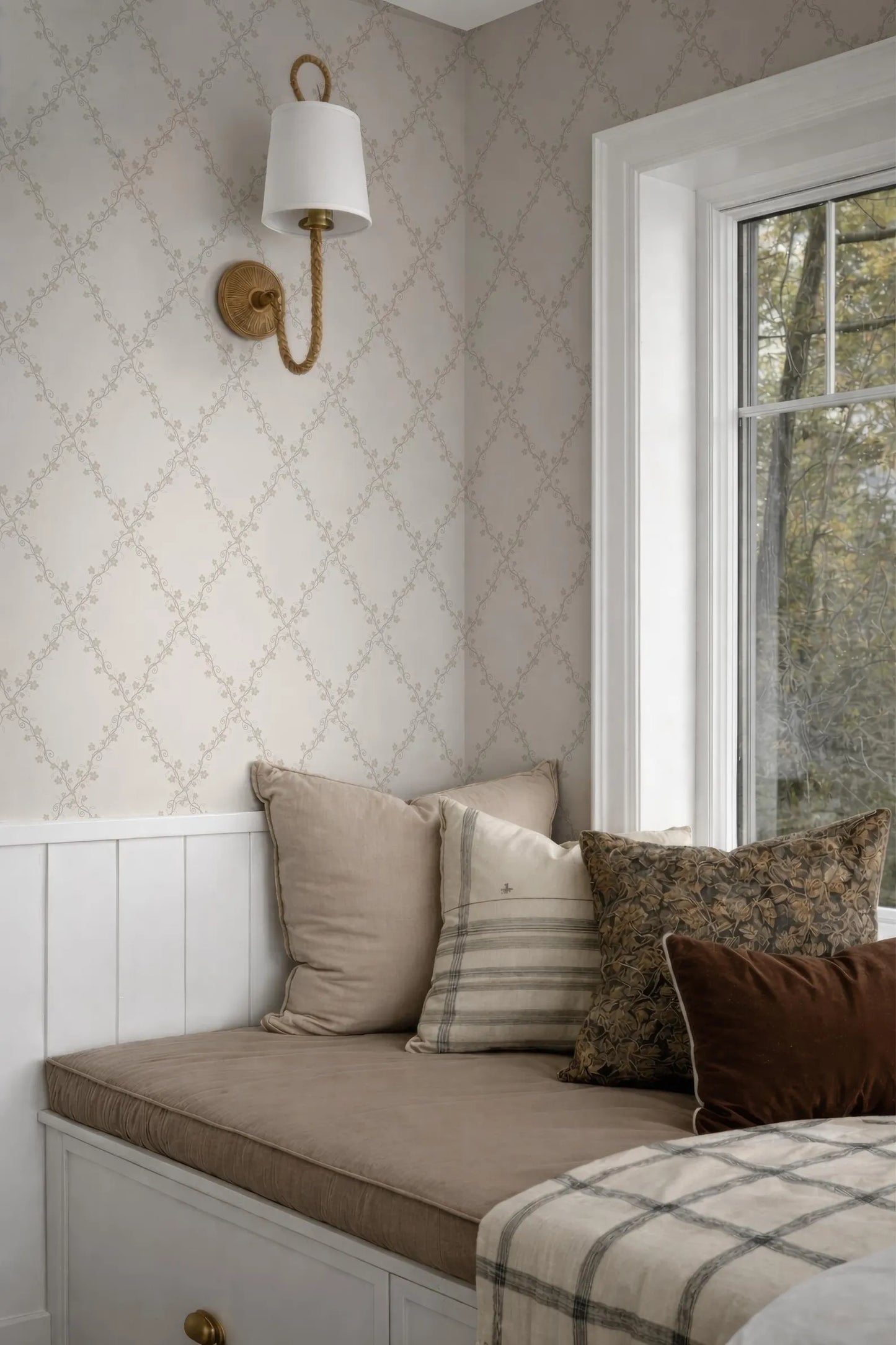 a cozy corner of a room with a white wall, a window, and a bed with a brown and white striped pillow.