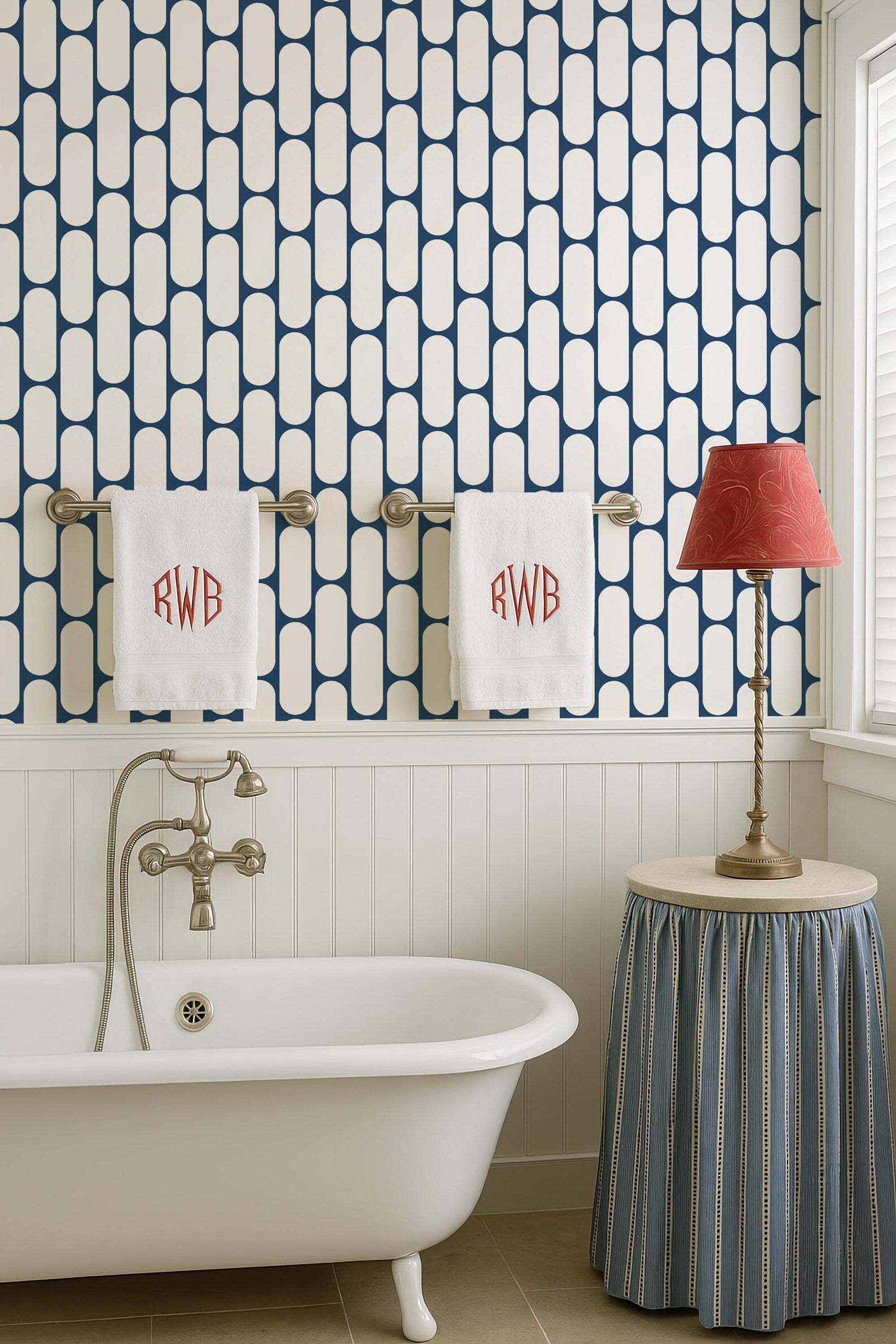 a bathroom with a white clawfoot bathtub, a towel rack with two towels, a red lamp, and a blue and white striped skirt.