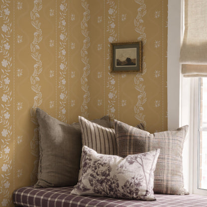 a cozy corner of a room with a window, a wall with a floral wallpaper, and a bed with a plaid pillow and a striped pillow.
