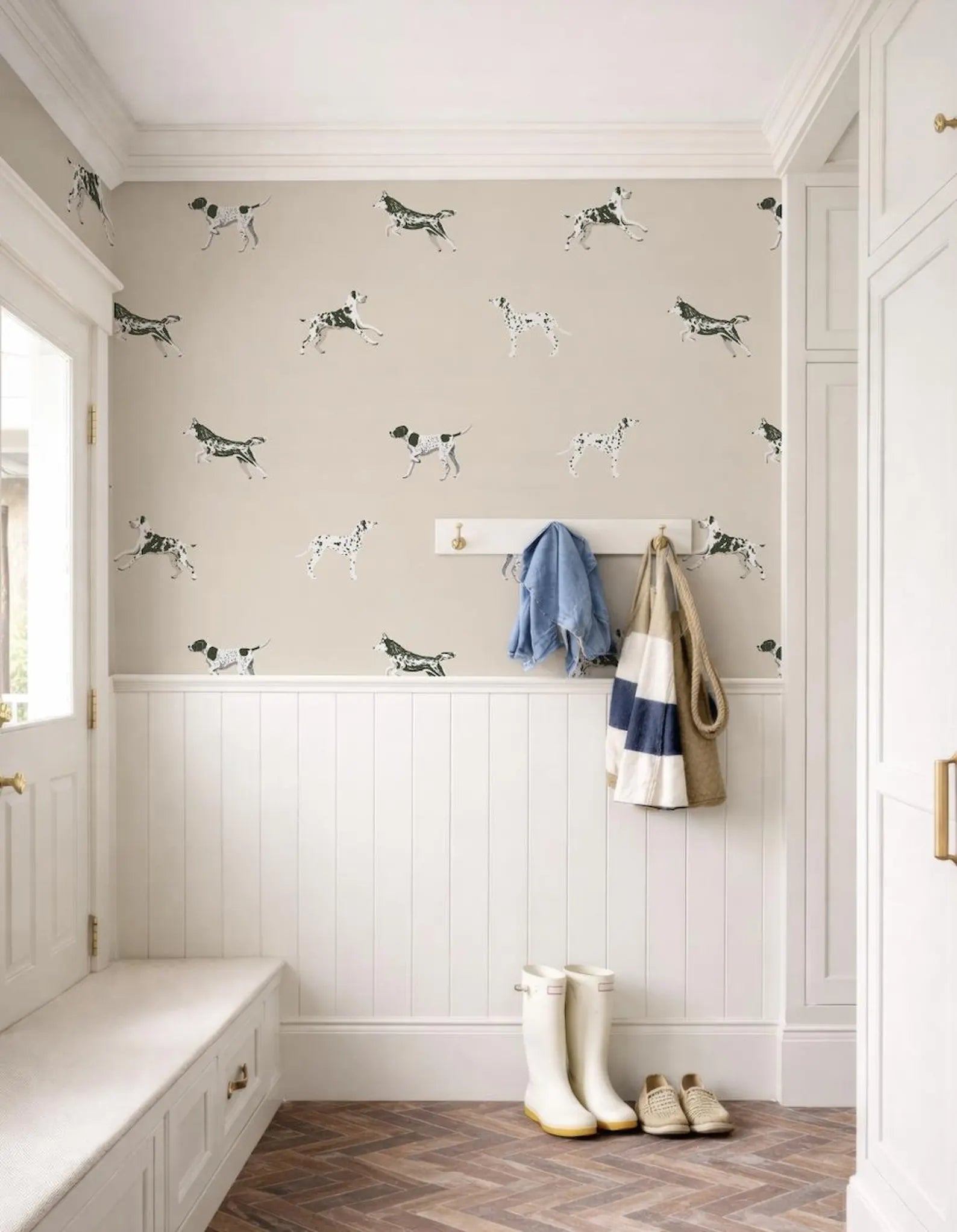 a hallway with a wallpapered wall adorned with a pattern of black and white dogs. A coat rack is mounted on the wall, and a pair of white boots is placed on the floor next to the coat rack.