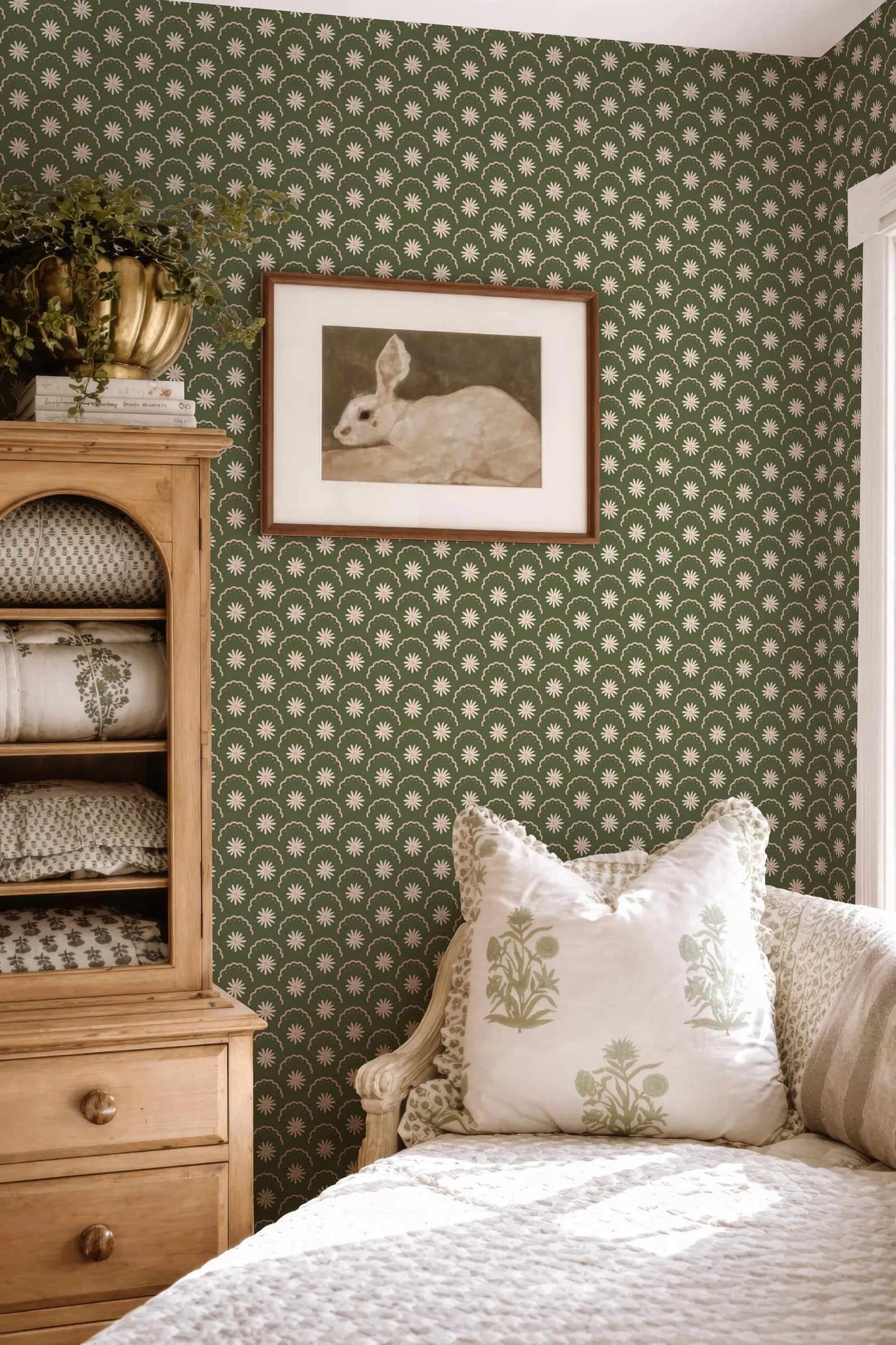 a cozy bedroom with a green and white patterned wallpaper, a wooden dresser, a framed picture of a rabbit, and a white sofa with decorative pillows.