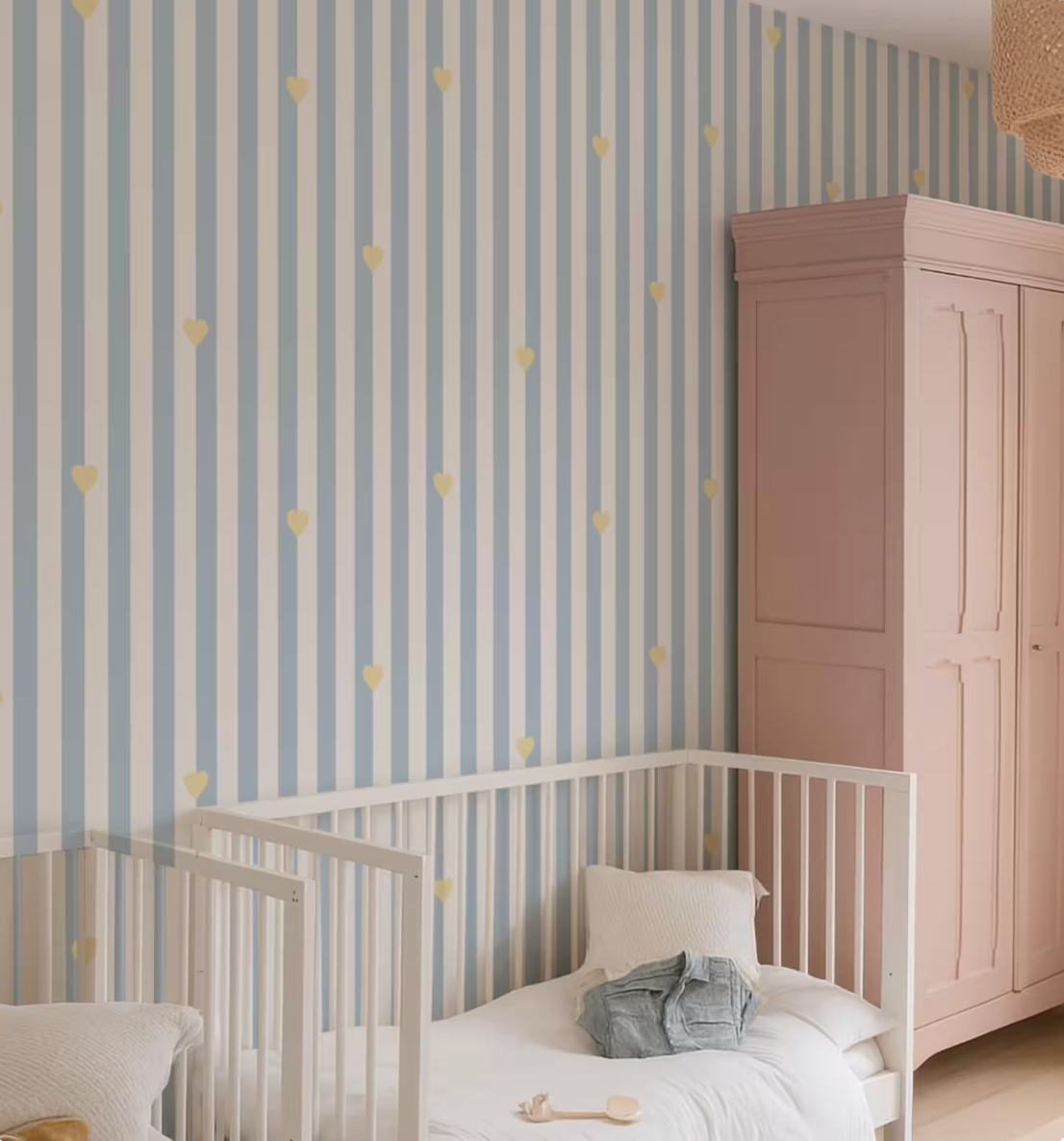 a cozy nursery room with a white crib, a pink wardrobe, and a striped wallpaper with yellow heart patterns.