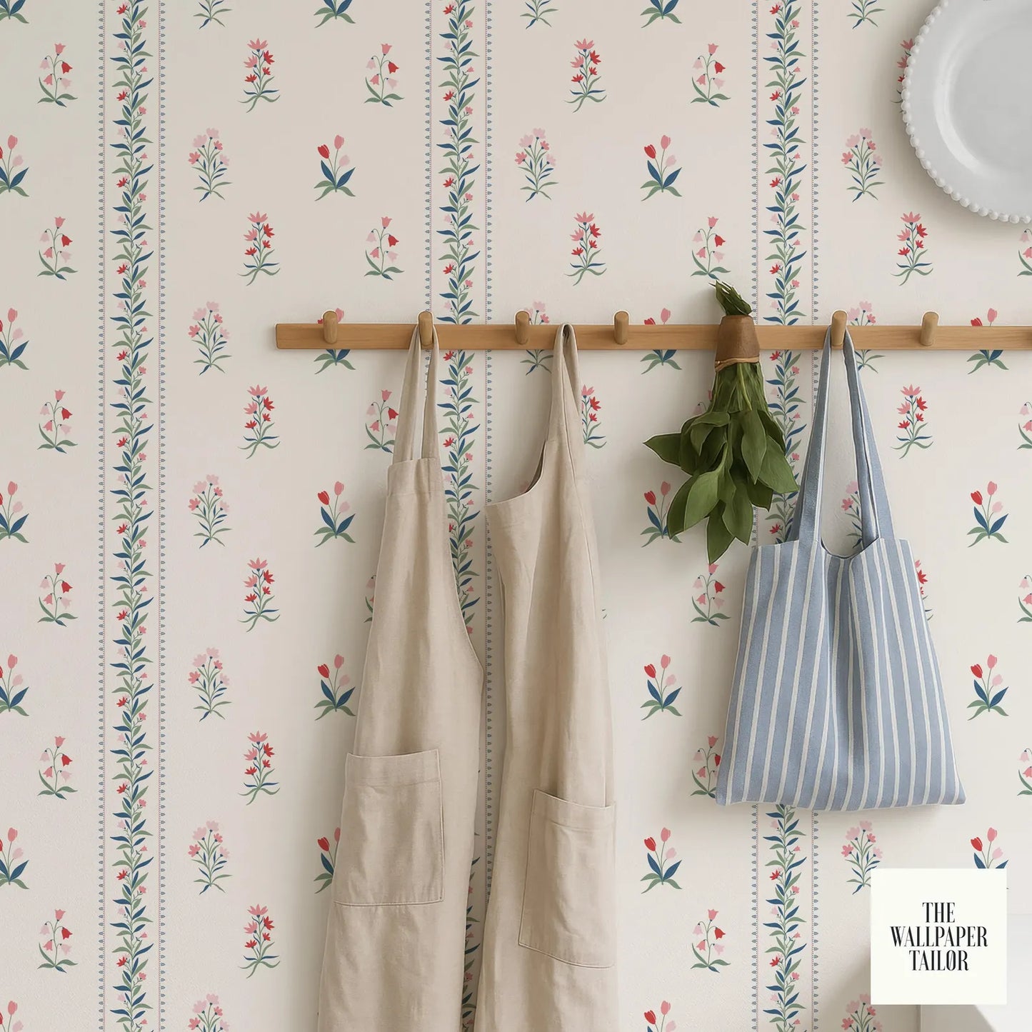 a wallpapered wall with a wooden rack holding a pair of beige aprons and a striped tote bag.