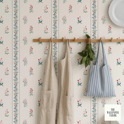 a wallpapered wall with a wooden rack holding a pair of beige aprons and a striped tote bag.