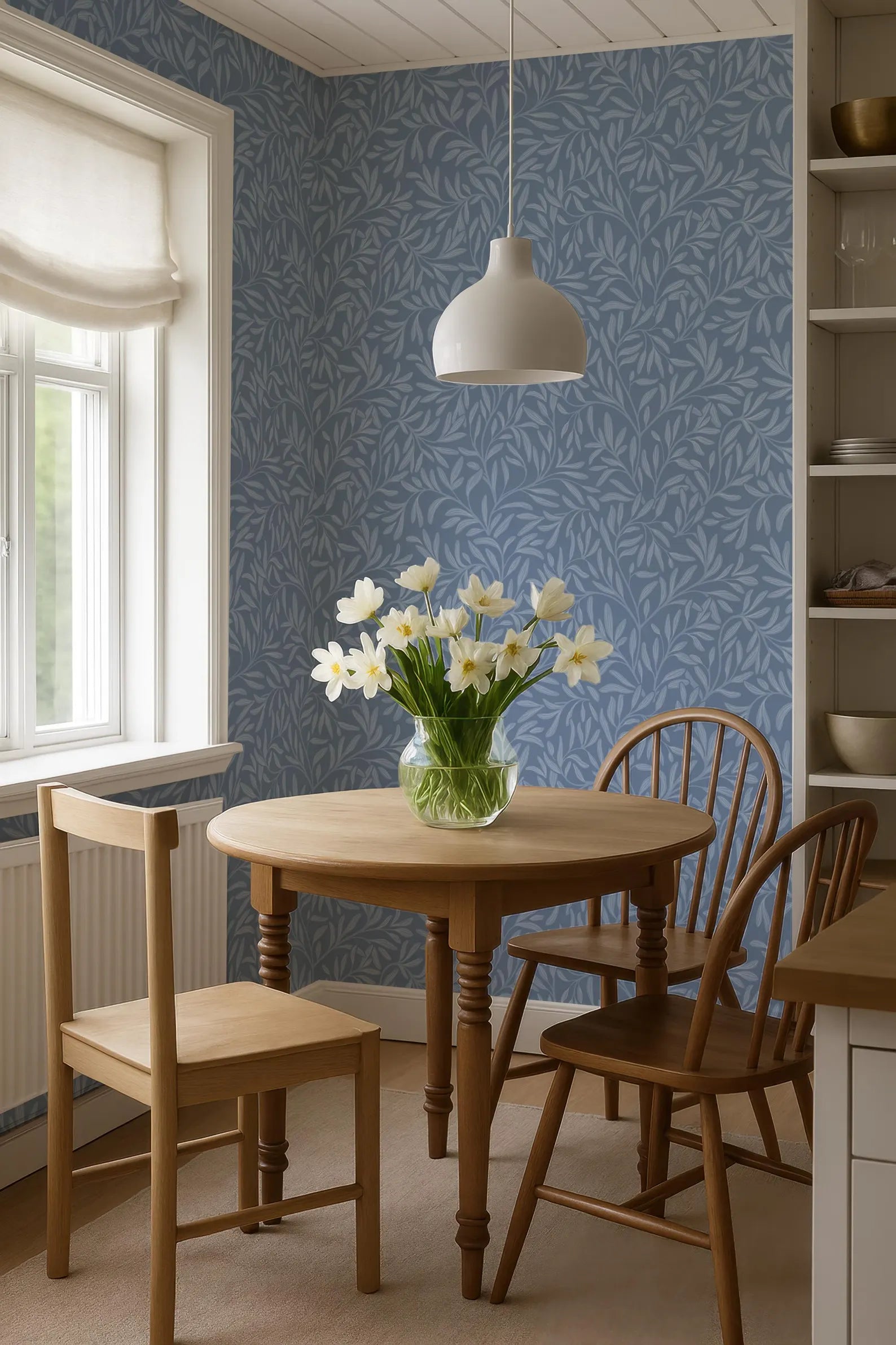a cozy dining area with a wooden table, two chairs, and a vase of white flowers on the table. The room has a blue and white patterned wallpaper, and a white pendant light hangs above the table.