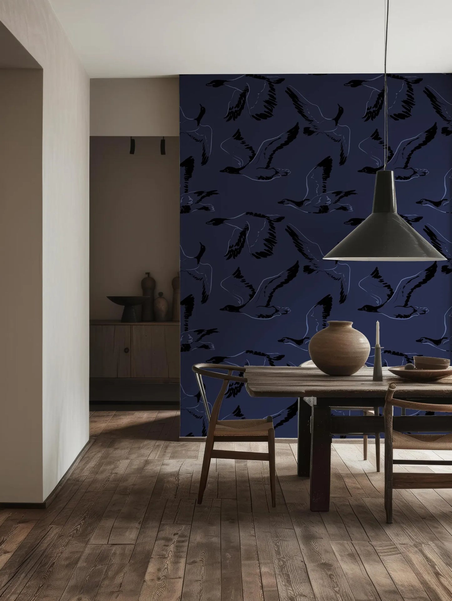 a dining room with a wooden table and chairs, a large wall with a patterned wallpaper, and a hanging light fixture above the table.