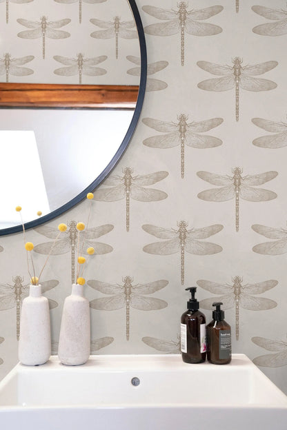 a bathroom setting with a white sink, a round mirror, and a wallpapered wall with a repeating pattern of dragonflies. There are two white vases with yellow flowers on the counter, and two bottles of soap are placed next to the sink.