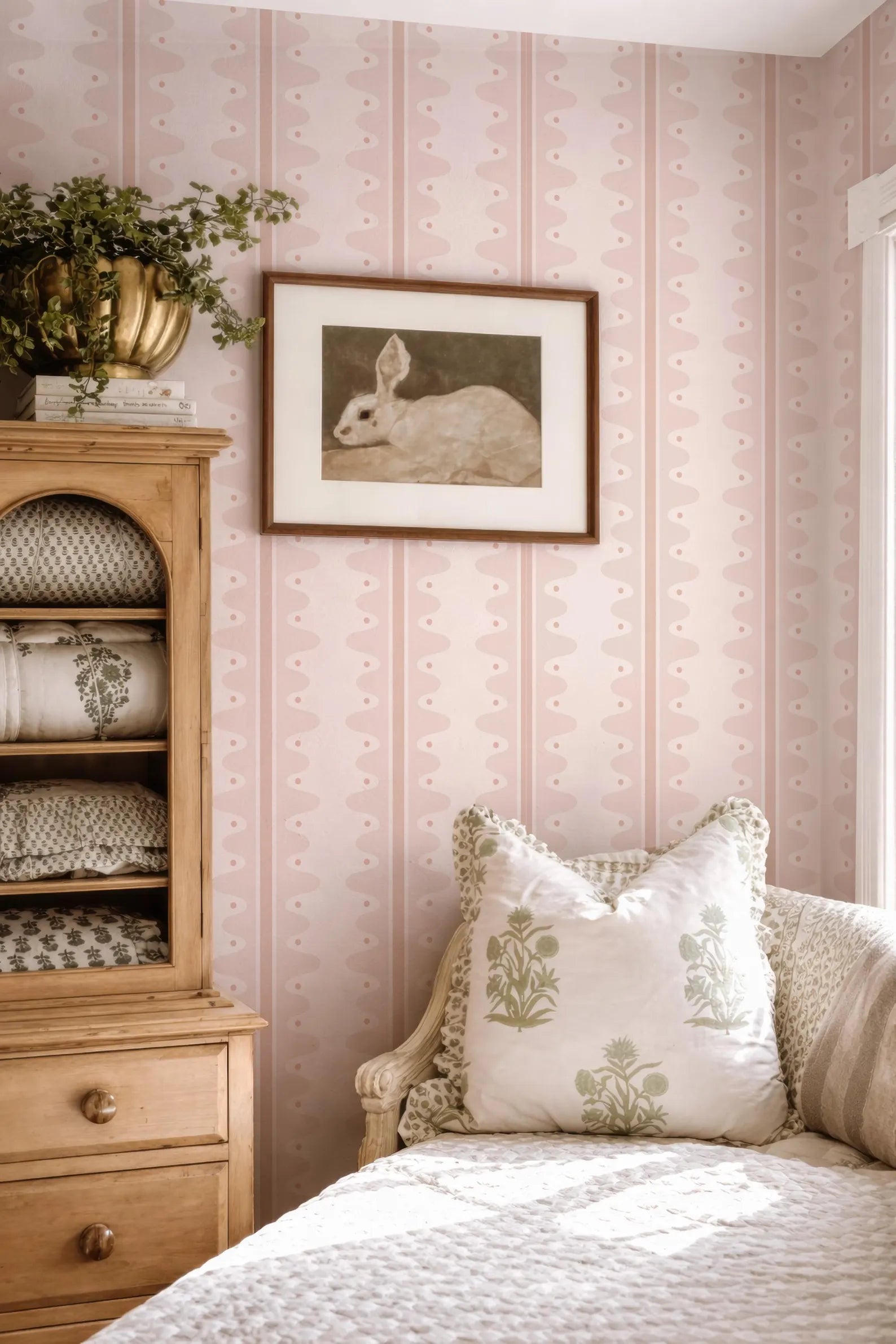 a cozy bedroom with a wooden dresser, a framed picture of a rabbit, and a white bed with decorative pillows.