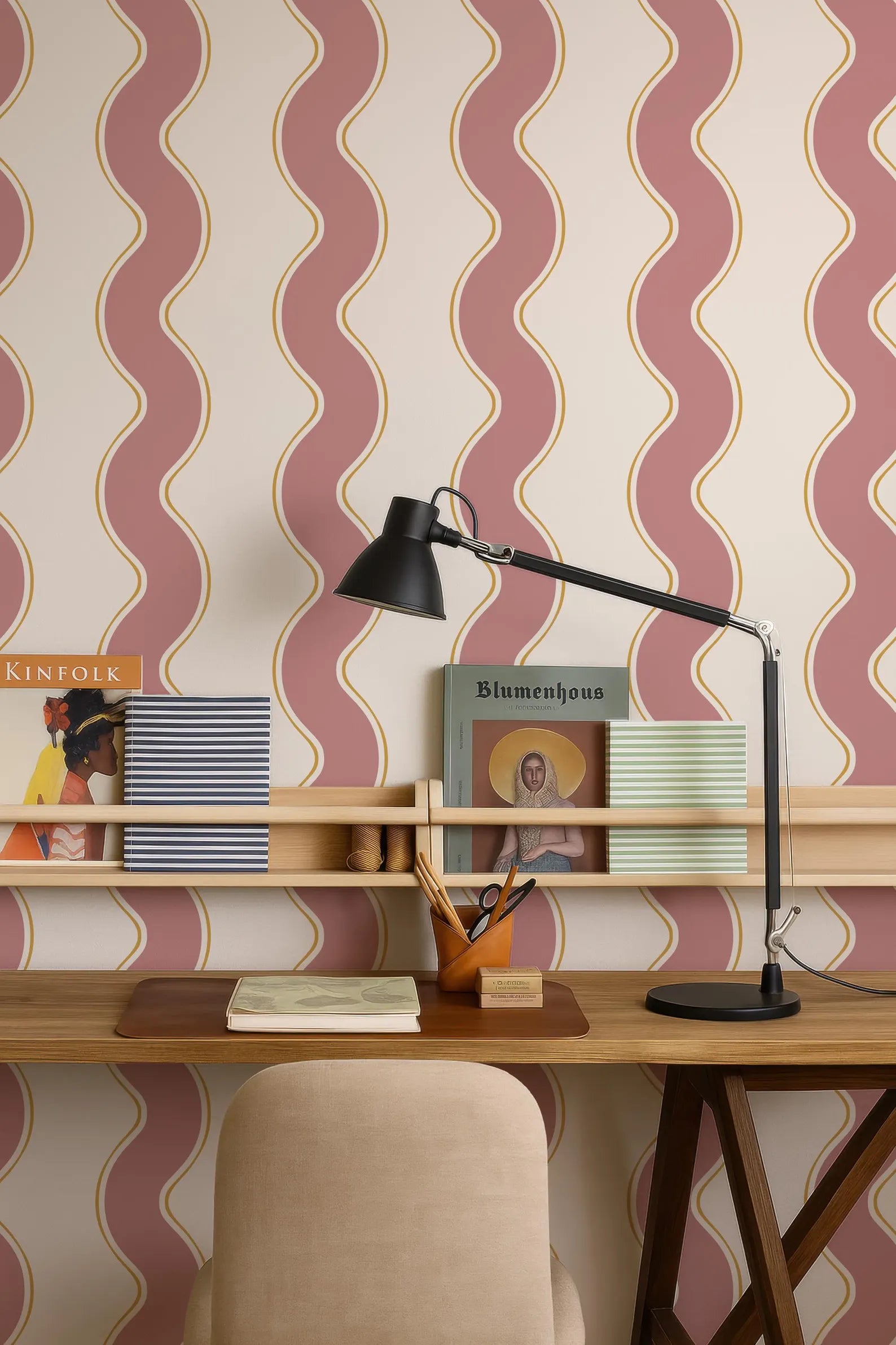 a wooden desk with a lamp, a book, and a magazine, set against a wall with a patterned wallpaper.