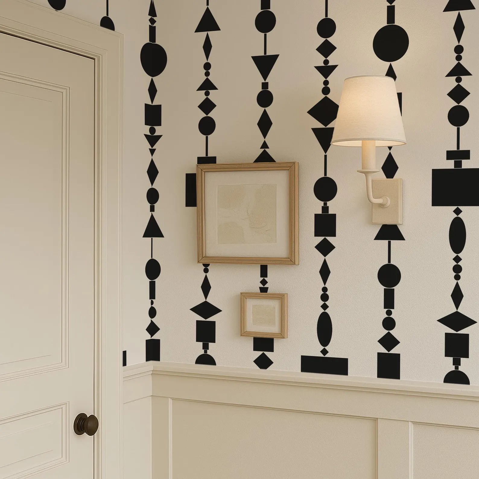 a wall with a black and white geometric pattern, including various shapes and designs. There is a framed picture hanging on the wall, and a wall lamp is also present in the scene.