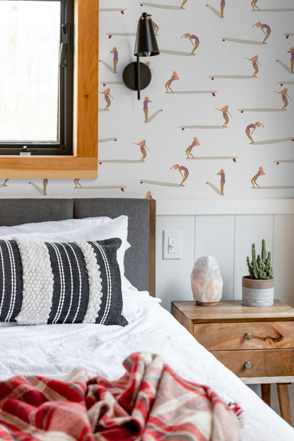 a bedroom with a bed, a nightstand, and a wallpapered wall featuring a repeating pattern of surfers.