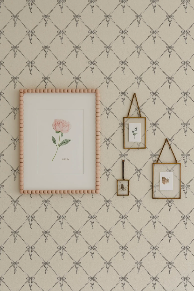 a wall with a framed picture of a rose, two smaller framed pictures, and a larger framed picture with a bow design. The wall has a patterned wallpaper with a repeating diamond design.
