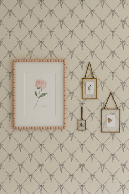 a wall with a framed picture of a rose, two smaller framed pictures, and a larger framed picture with a bow design. The wall has a patterned wallpaper with a repeating diamond design.