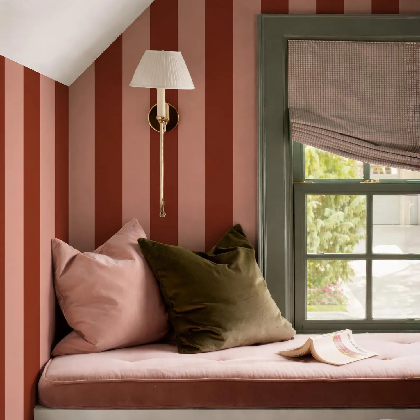 a cozy corner of a room with a window, a lamp, and a comfortable bed with pillows.