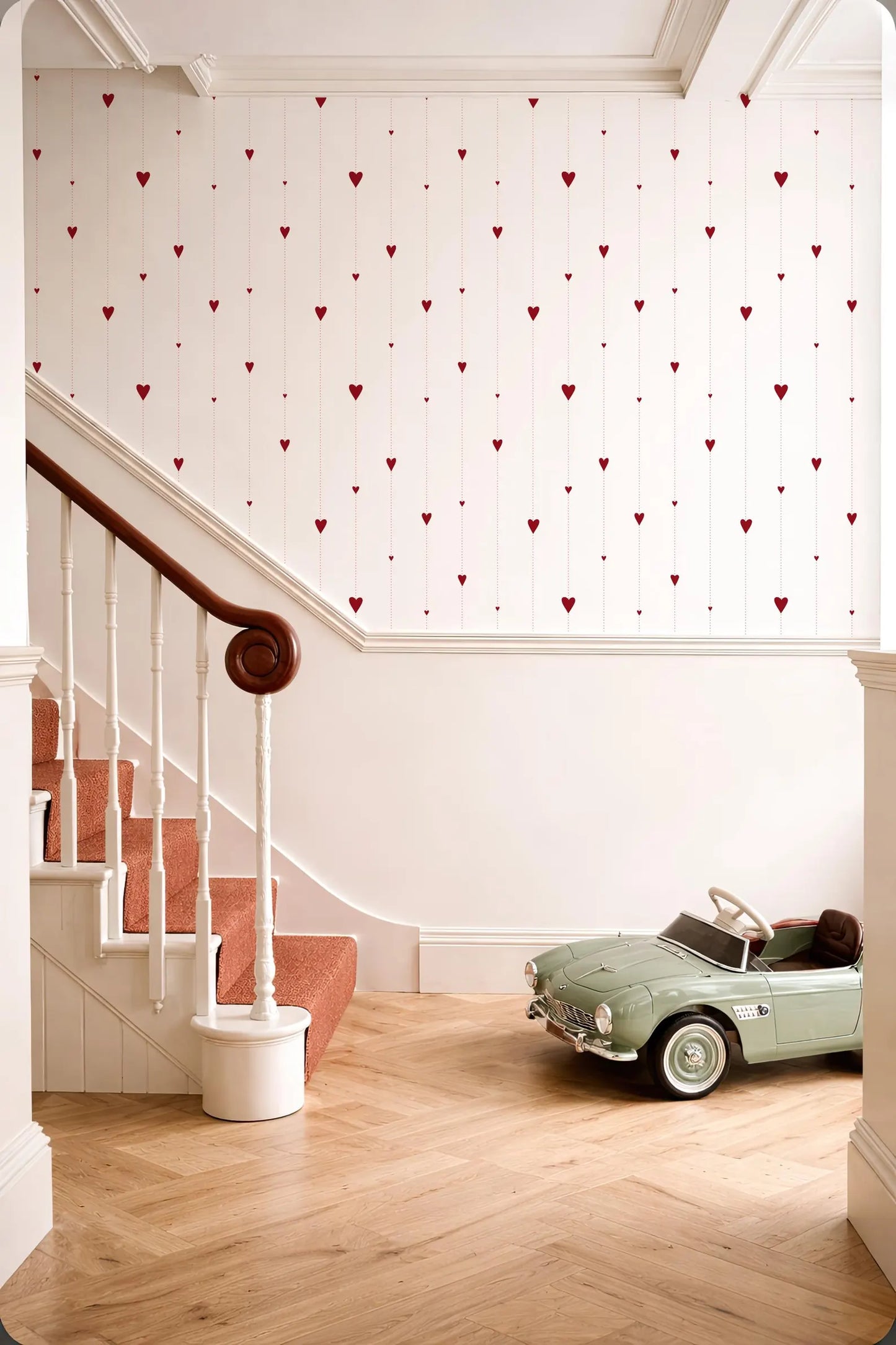 a vintage green toy car parked on a wooden floor next to a staircase with a white railing. The walls are decorated with red heart-shaped designs, creating a warm and inviting atmosphere.