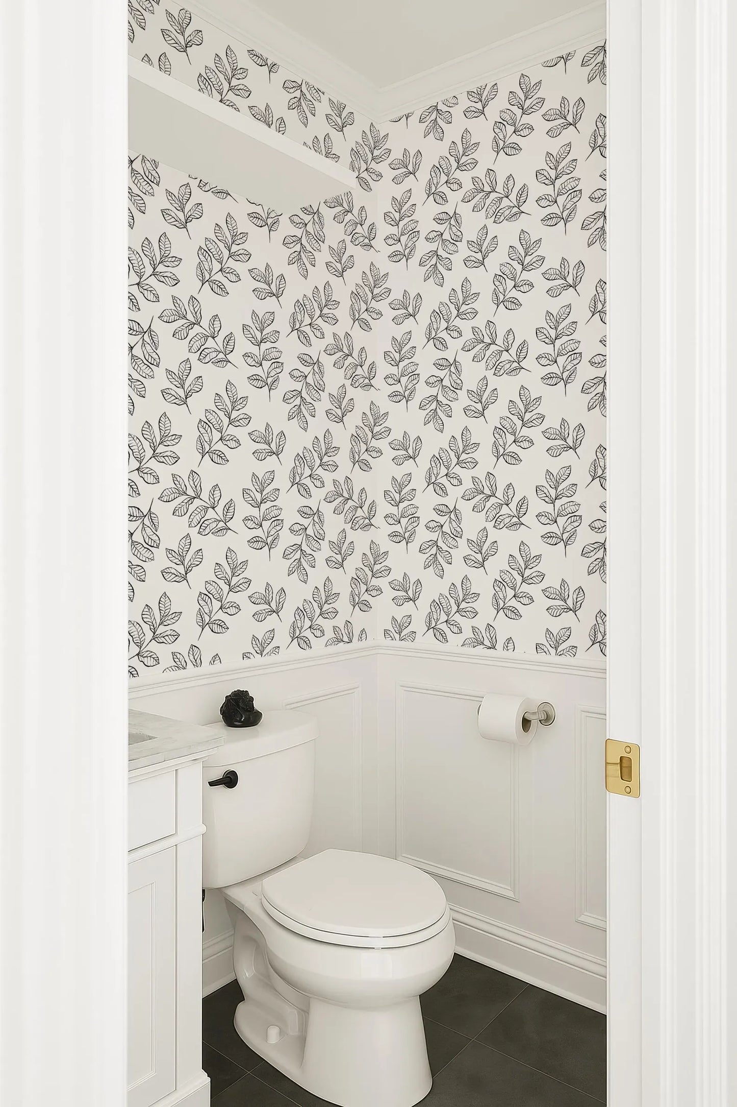 a bathroom with a white toilet and a white vanity. The walls are decorated with a black and white leaf pattern wallpaper.