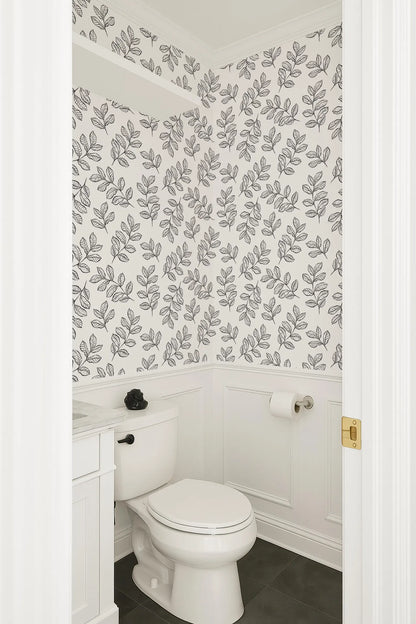 a bathroom with a white toilet and a white vanity. The walls are decorated with a black and white leaf pattern wallpaper.