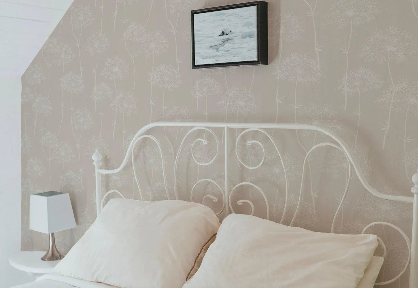a cozy bedroom with a white metal headboard and a white bed with two pillows. Above the bed, there is a framed picture hanging on the wall.