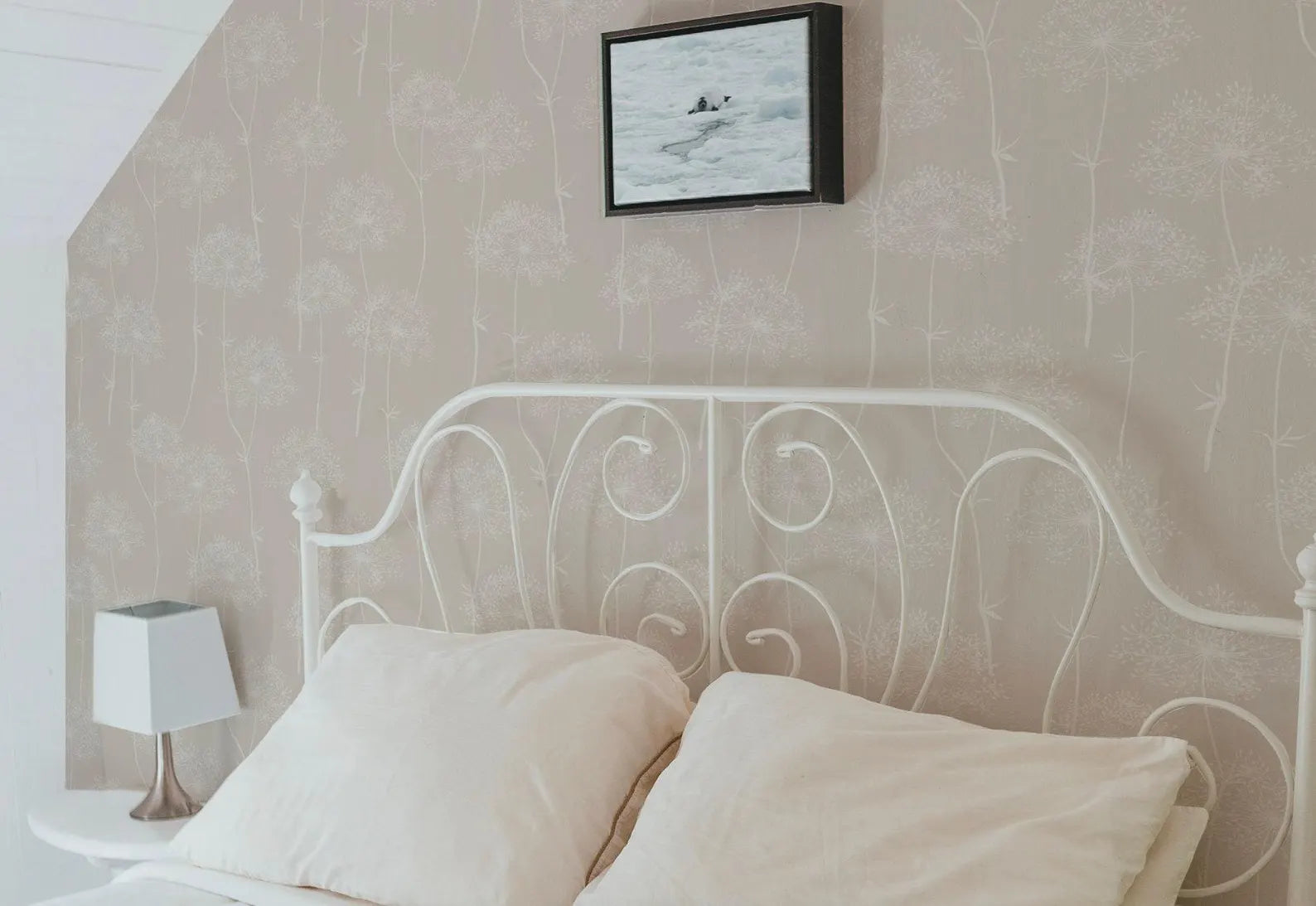 a cozy bedroom with a white metal headboard and a white bed with two pillows. Above the bed, there is a framed picture hanging on the wall.