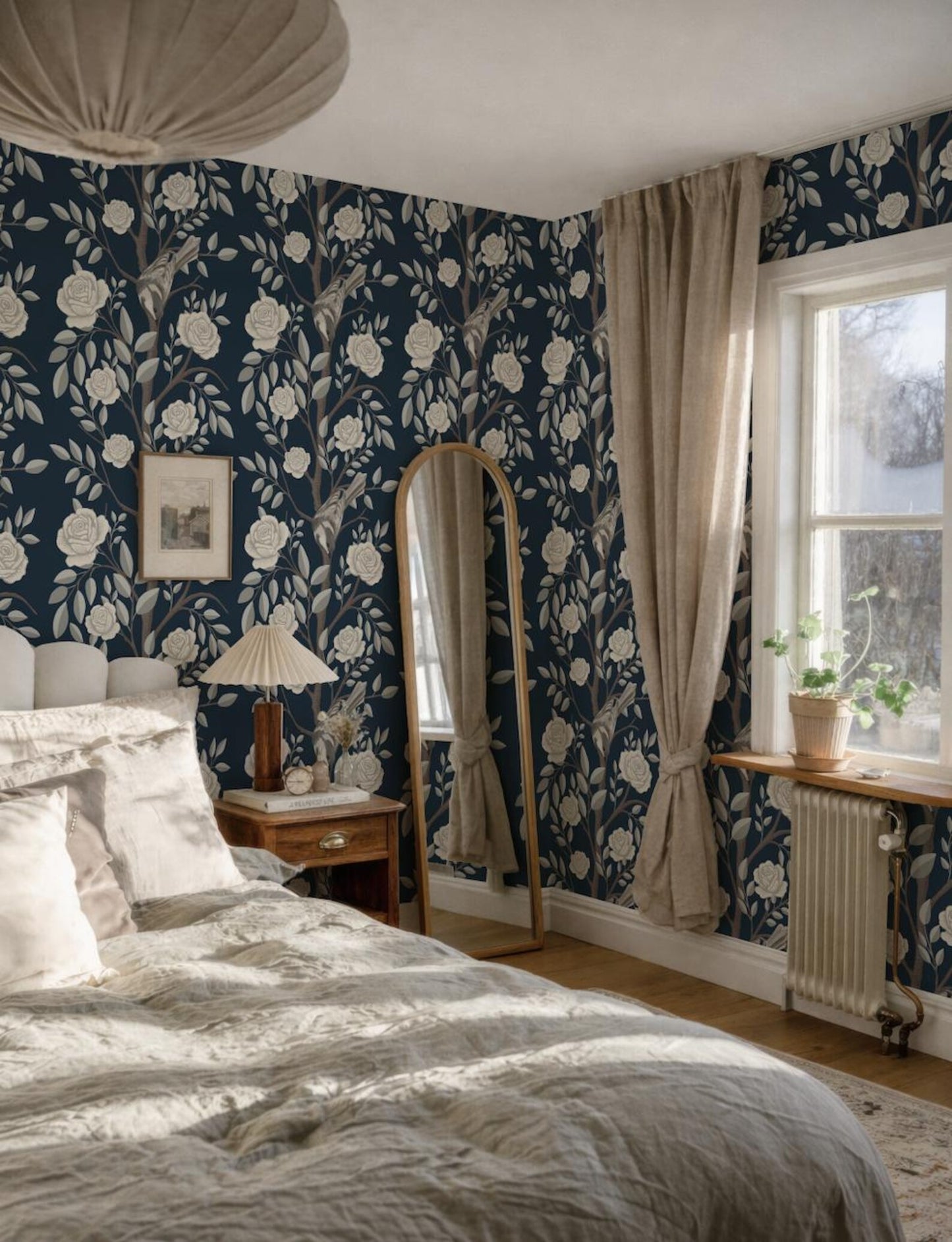 a cozy bedroom with a large bed, a mirror, a lamp, and a window with curtains. The walls are covered in a floral wallpaper, and the room has a warm, inviting atmosphere.