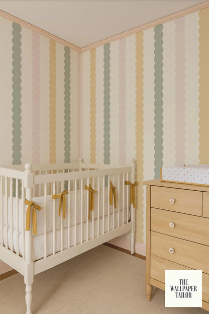 a nursery room with a white crib and a wooden dresser. The crib has yellow ribbons tied to it, and the walls are covered in a striped wallpaper with a pastel color palette.