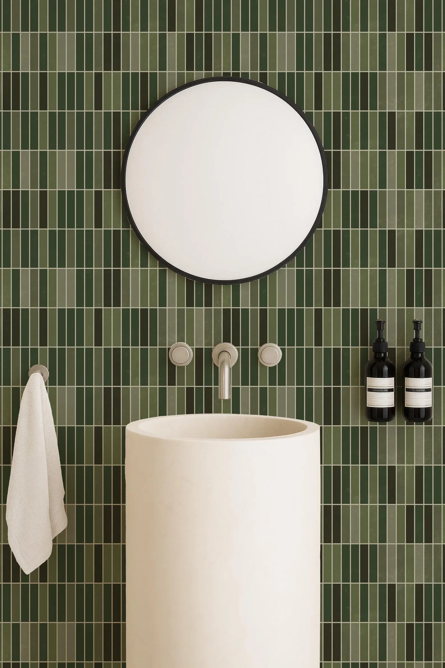 a bathroom with a white sink, a round mirror, and green tiles on the wall. There are also two bottles of soap on the wall.