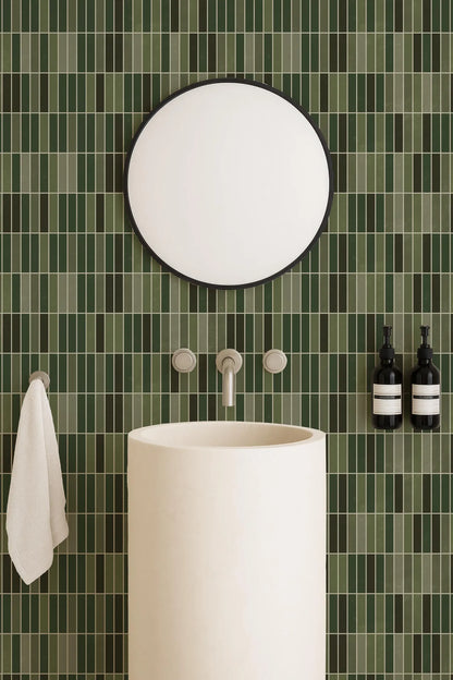a bathroom with a white sink, a round mirror, and green tiles on the wall. There are also two bottles of soap on the wall.
