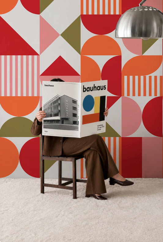 A person is sitting in a chair, reading a magazine or book titled "bauhaus" while wearing a brown suit.