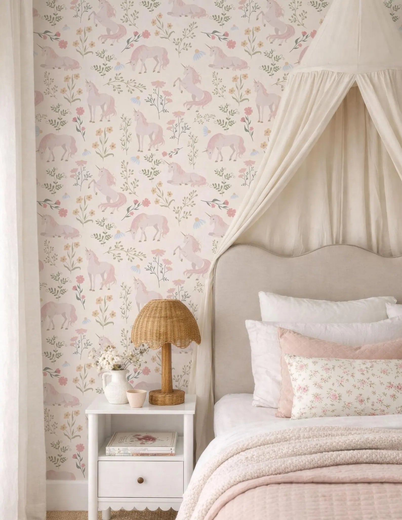 a bedroom with a canopy bed, a white nightstand, and a floral wallpaper. The room has a pink and white color scheme, with a canopy above the bed and a canopy lamp on the nightstand.