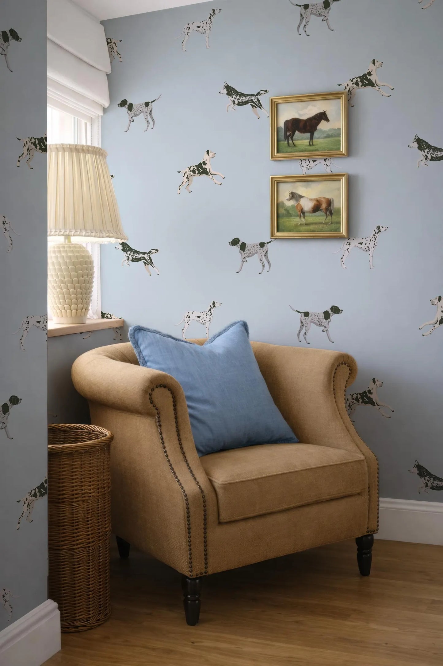 a cozy corner of a room with a beige armchair, a wicker basket, and a framed picture of a horse and a dog on the wall.