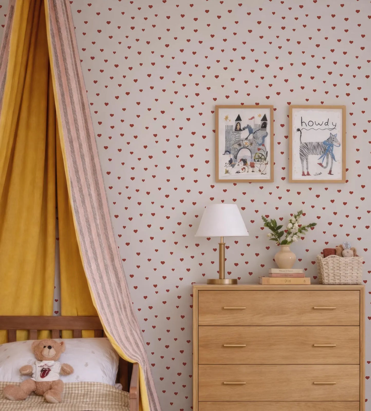 a cozy and charming bedroom scene, featuring a yellow canopy bed with a teddy bear, a wooden dresser with a lamp, and two framed pictures on the wall.