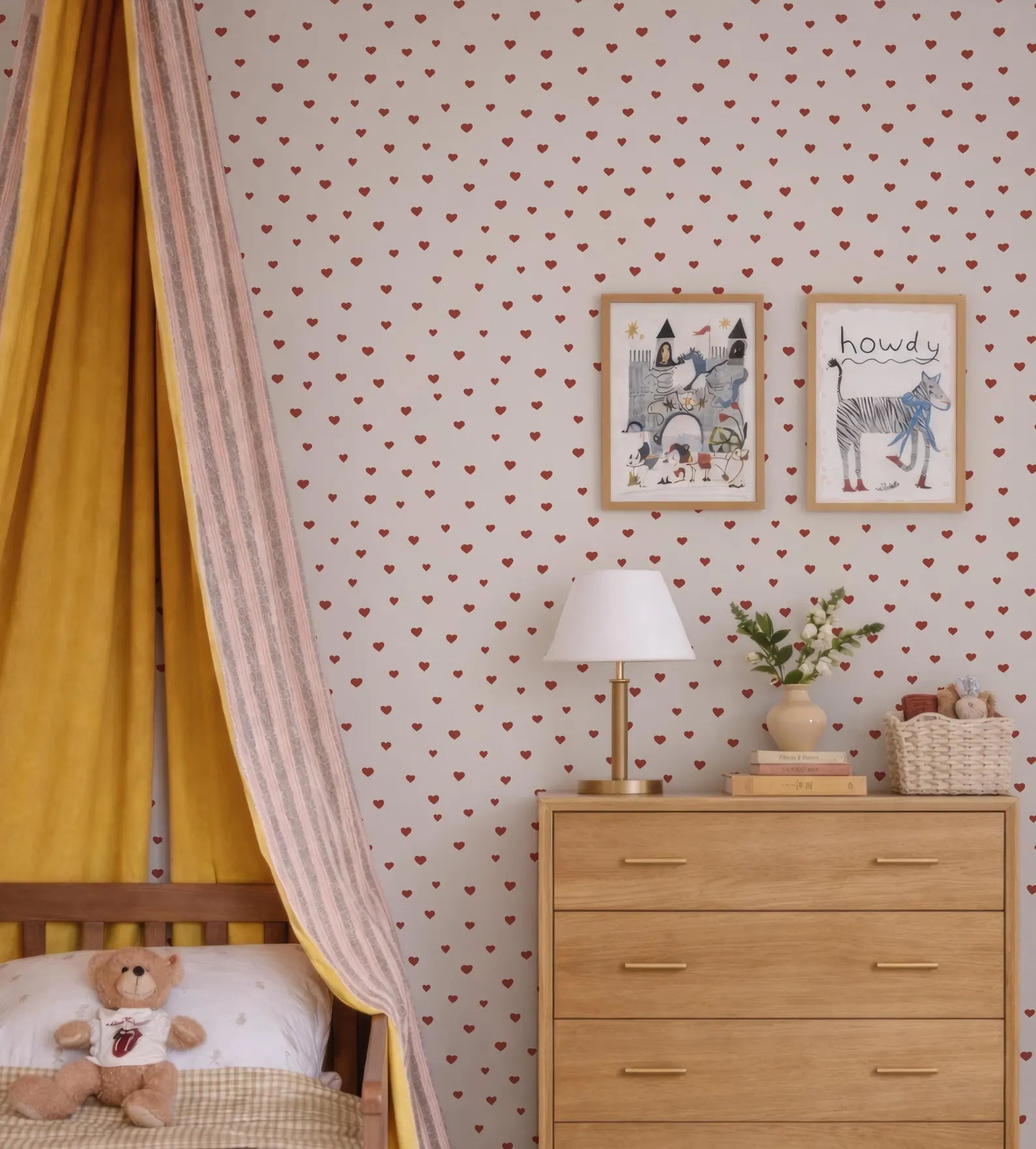 a cozy and charming bedroom scene, featuring a yellow canopy bed with a teddy bear, a wooden dresser with a lamp, and two framed pictures on the wall.