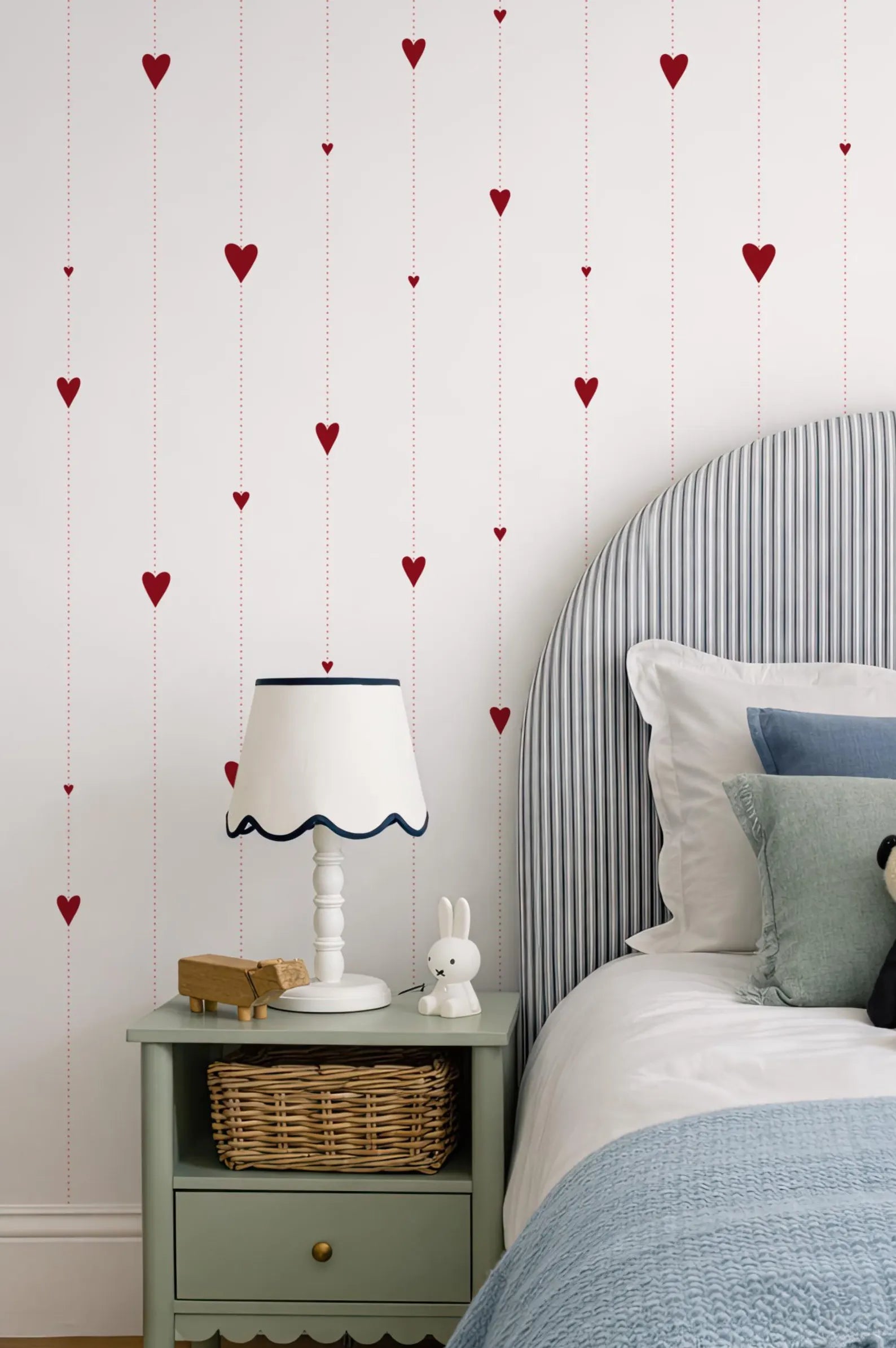 a cozy bedroom scene with a bed, nightstand, and heart-shaped decorations on the wall.