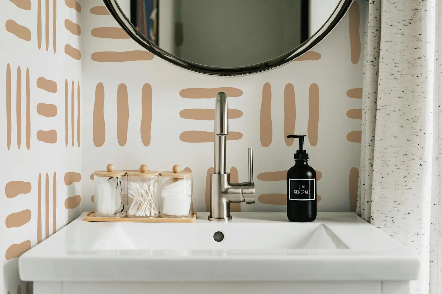 a bathroom sink with a black soap dispenser, a wooden tray with cotton swabs, and a round mirror above the sink.