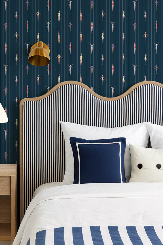 a bedroom with a striped headboard and a white bed with blue and white striped bedding. The wall behind the bed has a pattern of colorful figures, creating a vibrant and lively atmosphere.