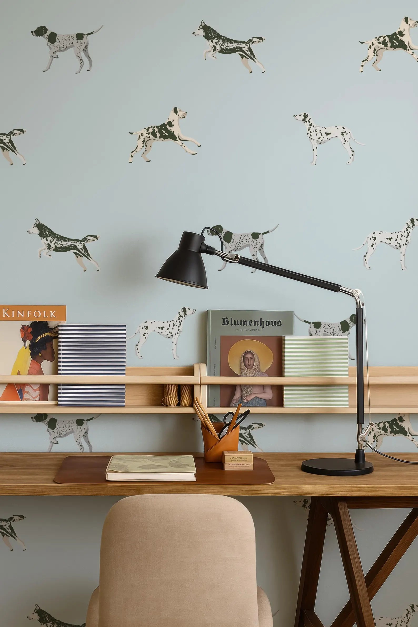 a workspace with a wooden desk, a lamp, and various items such as books and a magazine. The wall behind the desk has a pattern of dalmation dogs, adding a unique touch to the room's decor.