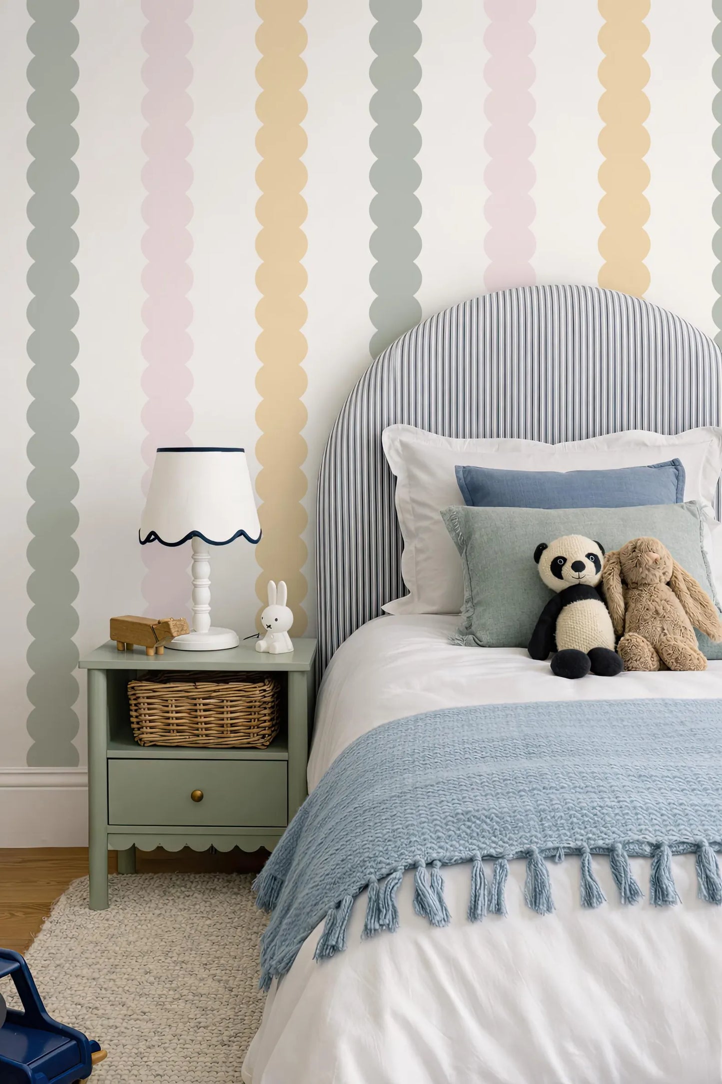 a cozy and colorful bedroom with a striped headboard, a blue blanket, and a nightstand with a lamp and a stuffed panda bear.