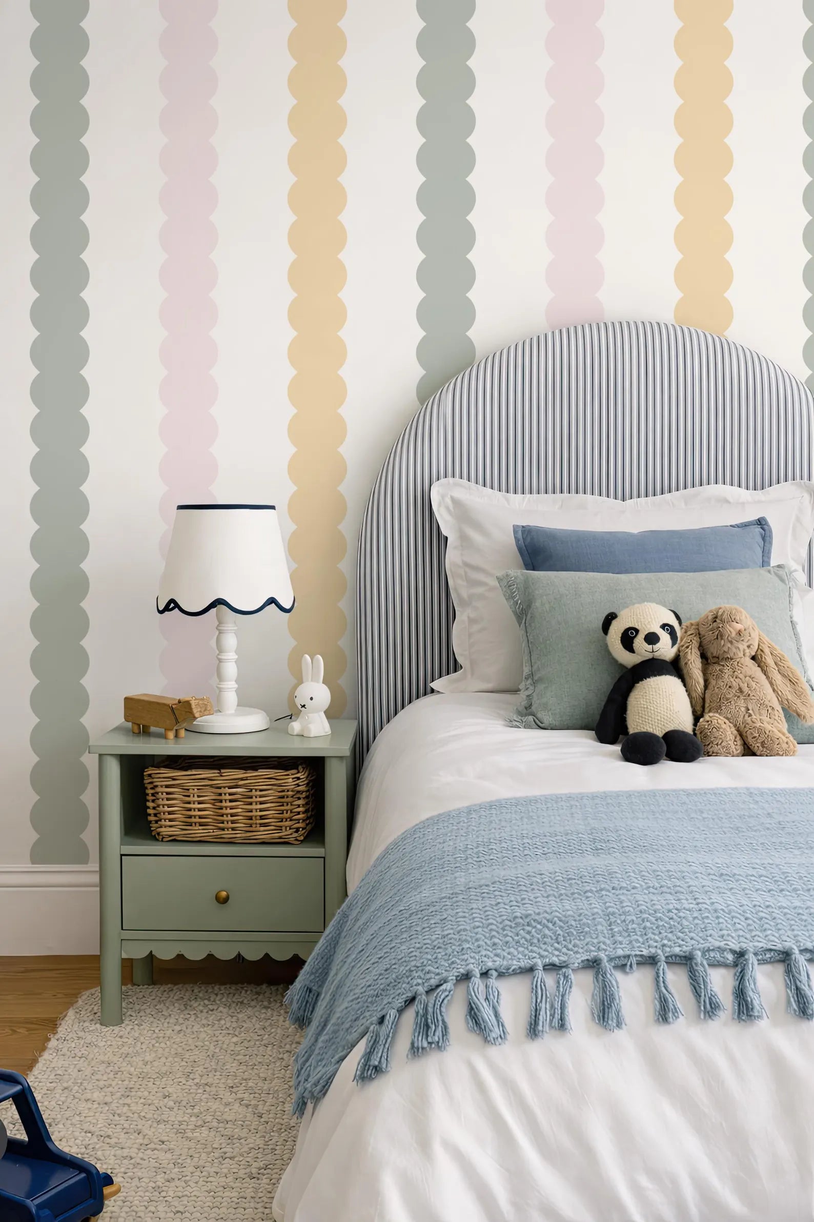 a cozy and colorful bedroom with a striped headboard, a blue blanket, and a nightstand with a lamp and a stuffed panda bear.