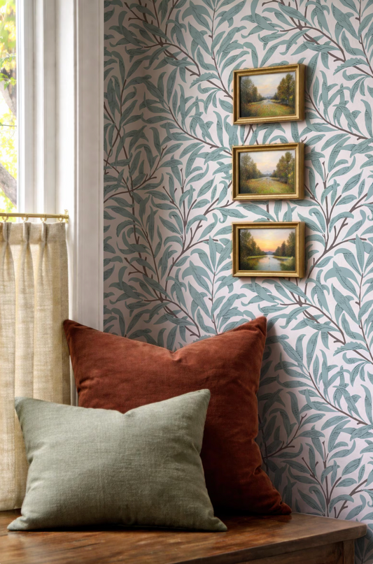 a cozy corner with a wooden table, a window with white curtains, and three framed pictures of landscapes hanging on the wall.