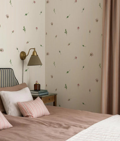a cozy bedroom with a bed, a nightstand, and a lamp. The walls are covered in a floral wallpaper, and the bed is dressed in pink and white bedding.