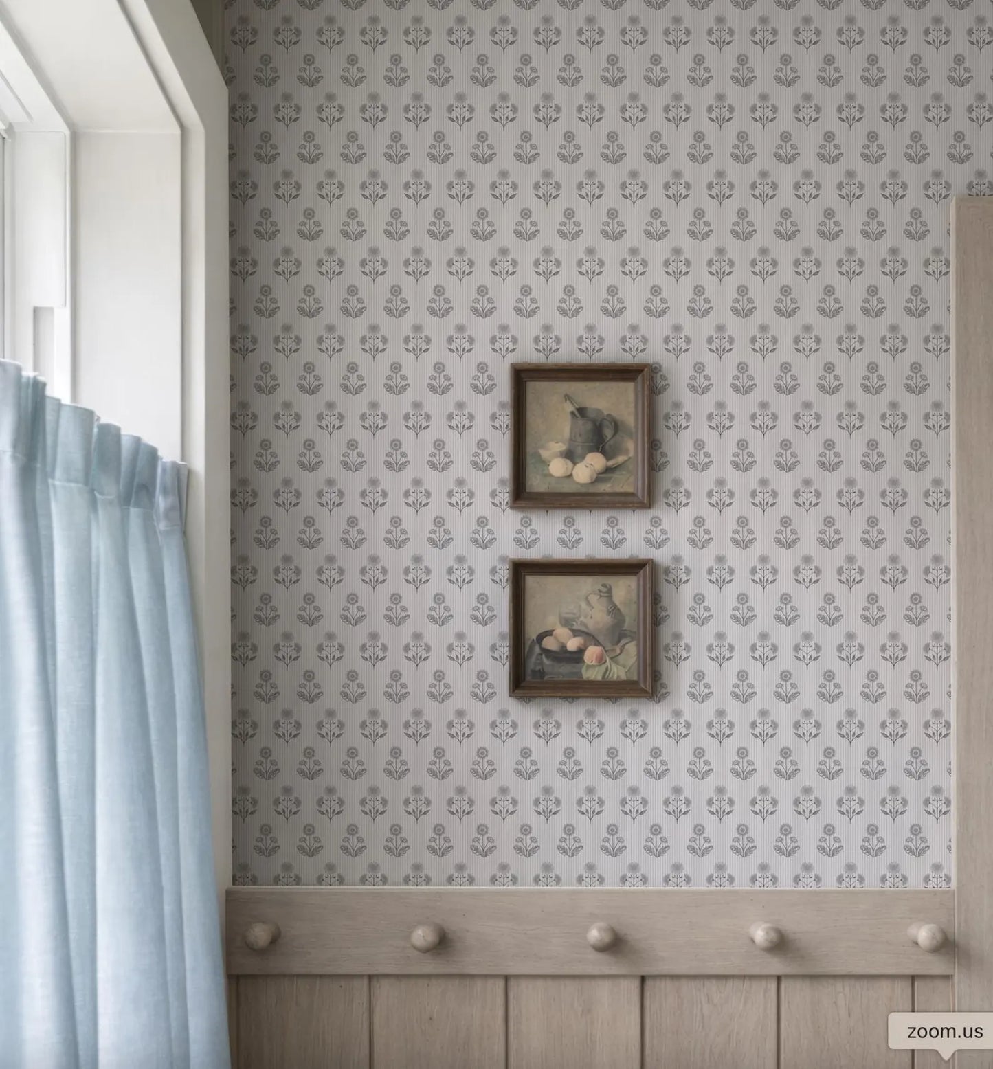 a wall with a patterned wallpaper and two framed pictures hanging on it. The wall is adjacent to a window with a blue curtain.