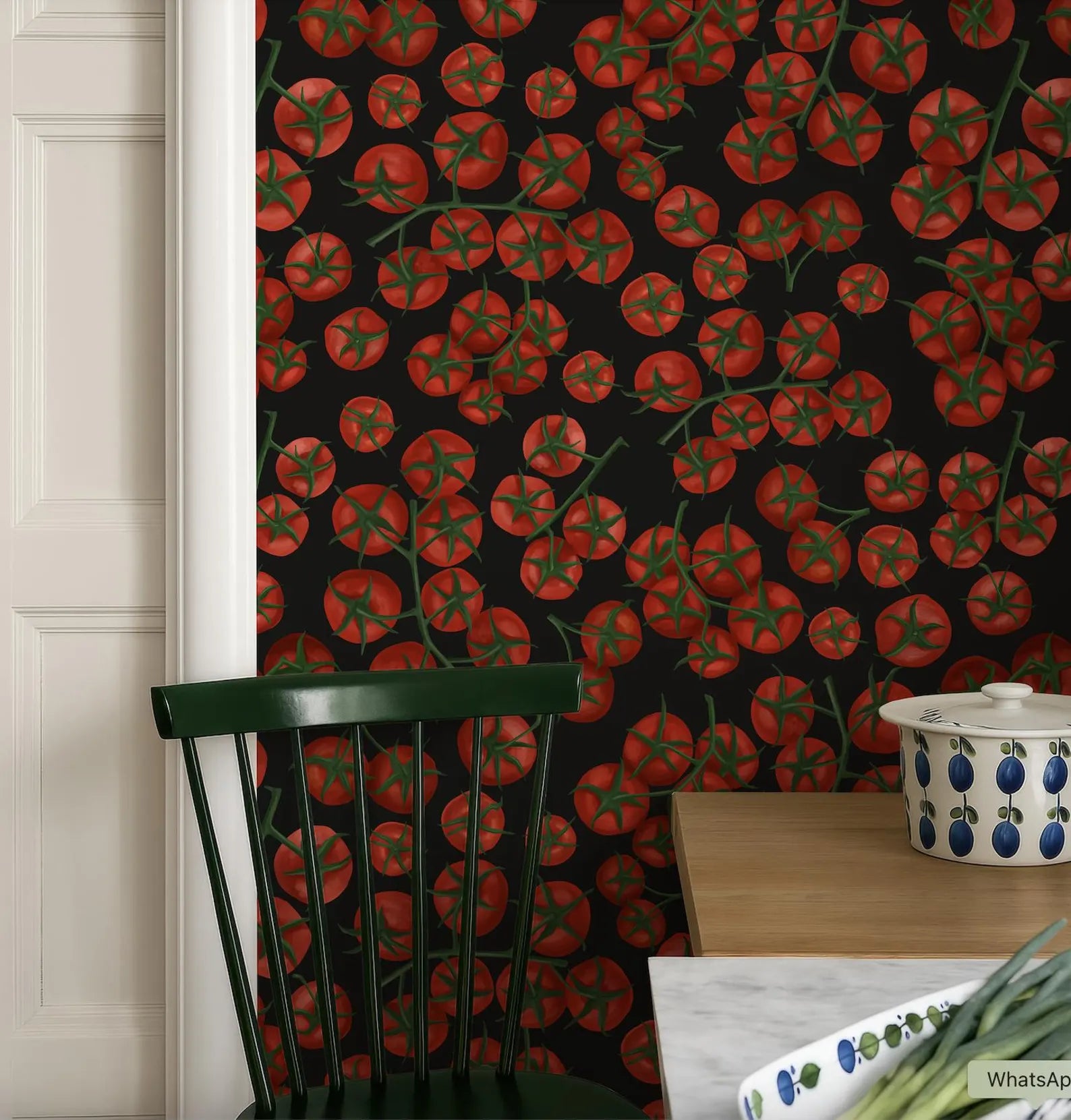 a kitchen scene with a black wall adorned with a vibrant tomato pattern. In the foreground, there is a green chair and a wooden table with a white bowl and a white plate.