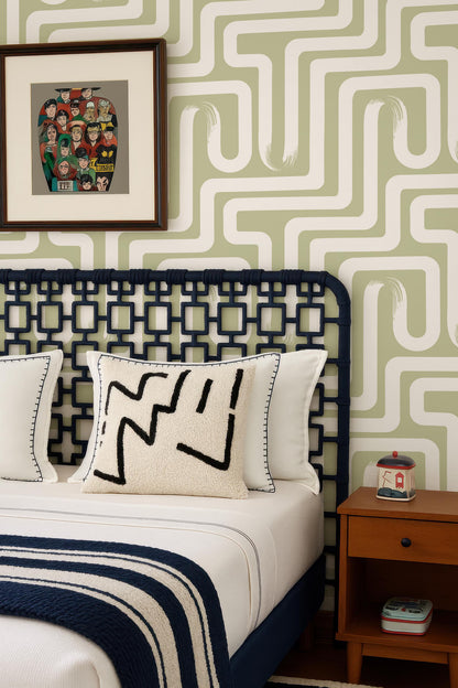 a bedroom with a bed, a framed artwork on the wall, and a wooden nightstand. The bed has a white comforter and a black and white patterned pillow. The wall has a green and white geometric pattern, and there is a small wooden table with a red and white container on it.