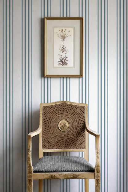a wooden chair with a woven seat, positioned against a striped wall. Above the chair, there is a framed artwork hanging on the wall.